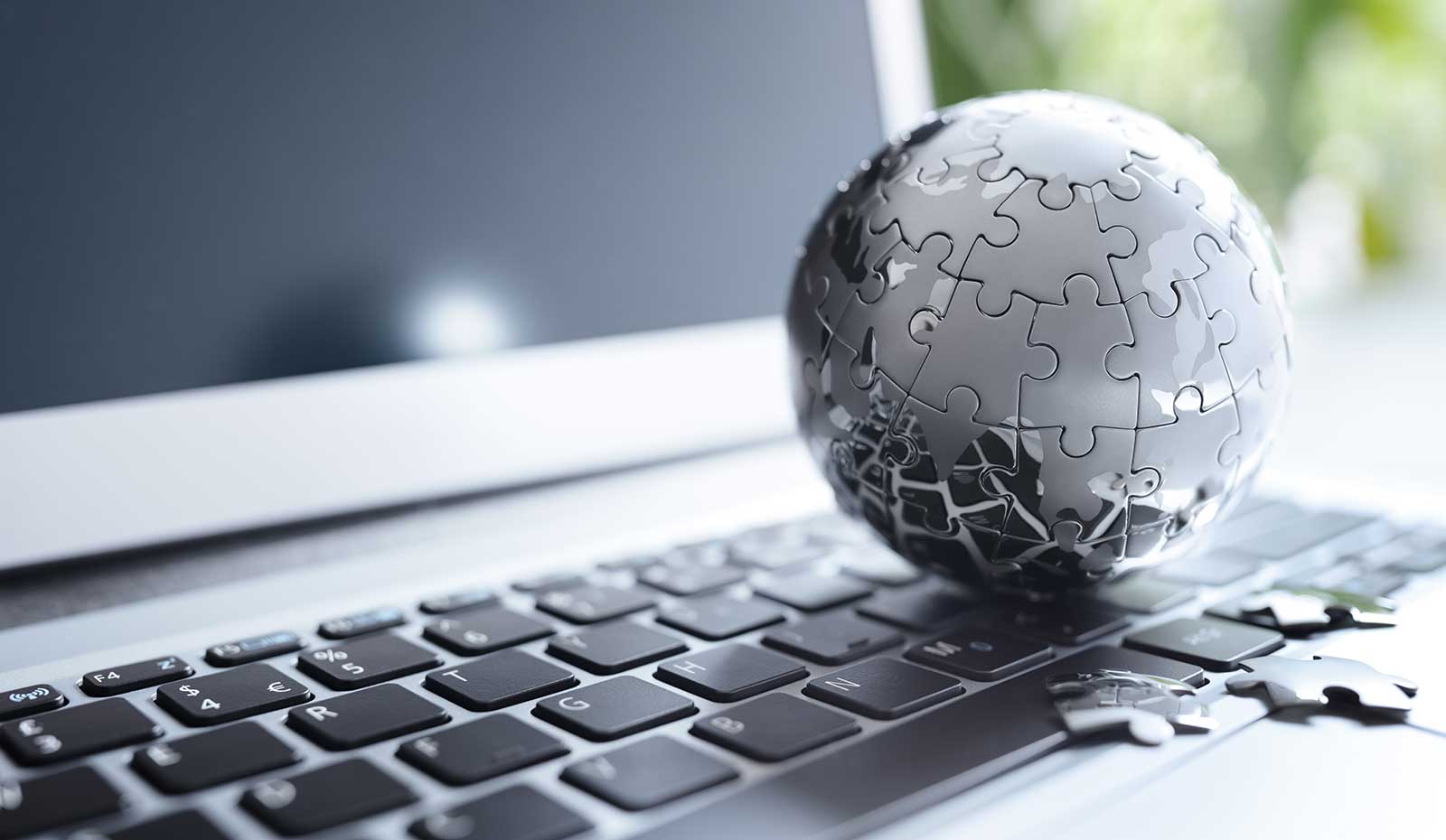 A globe made of puzzle pieces sitting on top of a laptop keyboard.