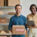 A smiling man holding a fragile shipping box standing next to a woman holding a tablet for shipping planning.