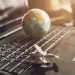 A small globe and airplane figurine arranged on a laptop's keyboard.